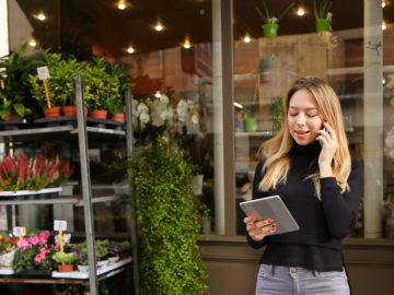 Female manager of flower shop standing with tablet and talking about green business funding